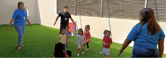 Maestra de CAYAM coordinando una actividad de juego y desarrollo motor con niños al aire libre.