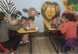 Personal educativo de CAYAM interactuando con niños en un aula decorada con murales de animales.