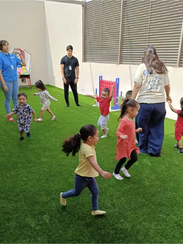 Niños jugando al aire libre en el área de juegos con pasto sintético del centro.